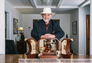 Daley with white hat and suit, standing behind his table with his new Emerald Whiskey on the table 