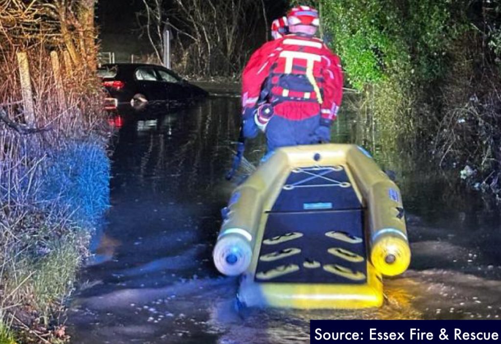 car stuck in flooded road, with rescue team approaching with inflatable raft