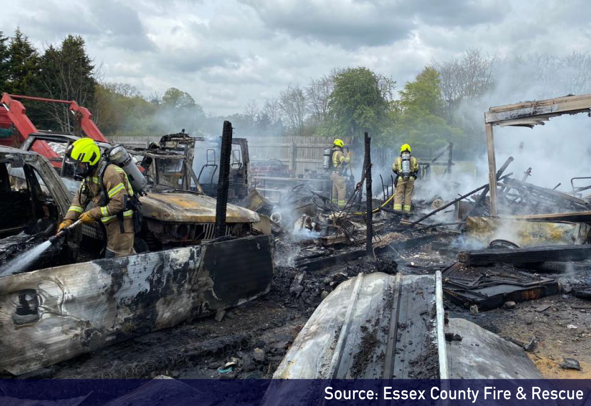 scene of burnt out vehicle at scrap yard, with fire fighters ensuring the fire is extinguished